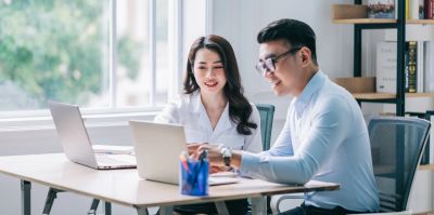 Two colleagues working together at laptops in an office.