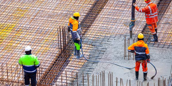 Construction workers pouring concrete on steel reinforcement at a building site.