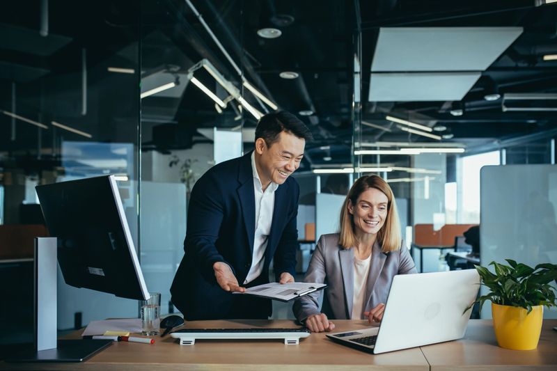 Two employees in a modern office, an Asian man and a woman working at a table, colleagues discussing and consulting, thinking about a joint project