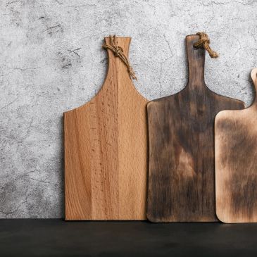 Three wooden cutting boards with different finishes leaning against a concrete wall.