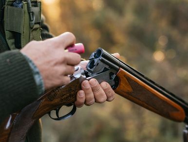 Man loading shotgun with a cartridge outdoors.