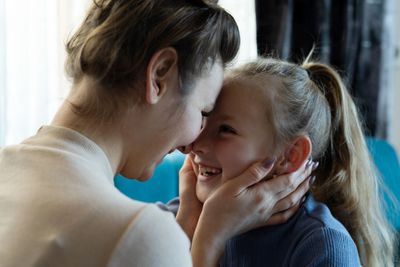 A smiling mother hugs her happy toddler on a couch.