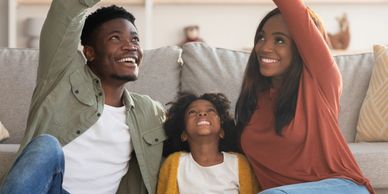 Happy family of three making a roof shape with their hands while sitting on the floor.