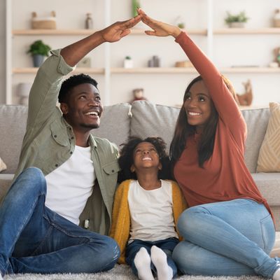 Happy family of three making a roof shape with their hands while sitting on the floor.