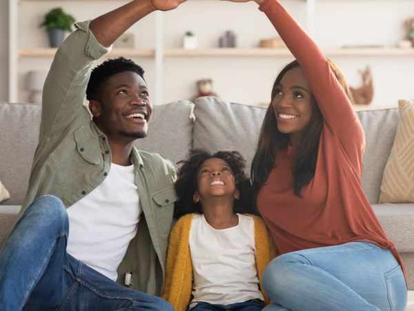 Happy family of three making a roof shape with their hands while sitting on the floor.