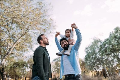 Two men and a child enjoying outdoors with trees and sky in the background.
