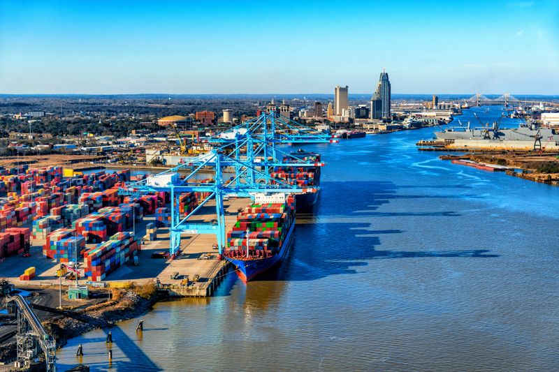 WIde angle view of the Port of Mobile, Alabama, with two fully loaded cargo ships moored at the docks, and the skyline of downtown up the river beyond.