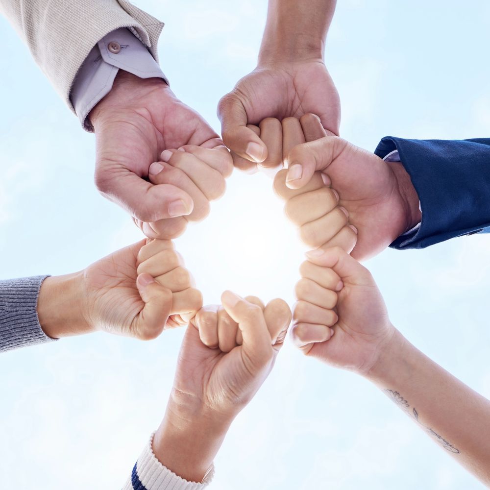 Group of diverse hands joining in a fist bump circle under a clear sky.