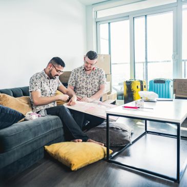 Two men in matching shirts unpacking a framed picture in a living room with moving boxes.