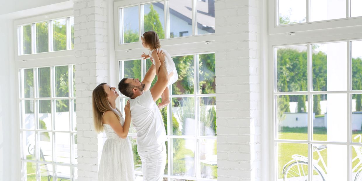 Couple holding baby in bright, sunlit room with large windows after professional house cleaning
