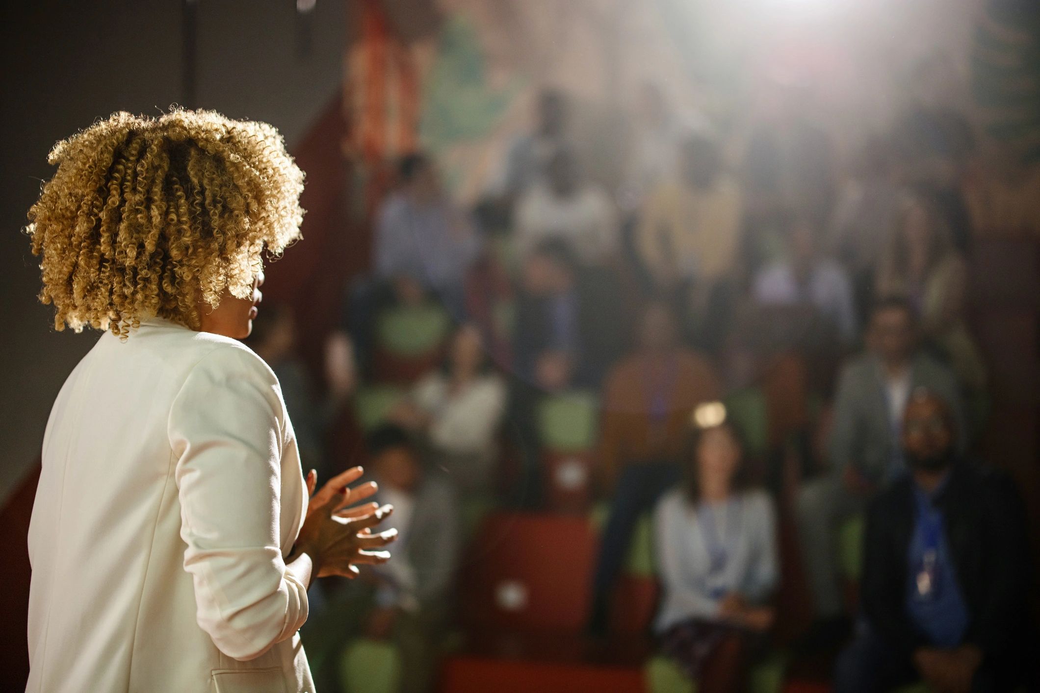 Woman speaking confidently to an audience in a dimly lit room.