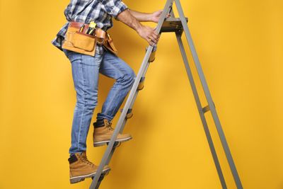 Person wearing boots climbing a metal ladder correctly for working at height regulations 