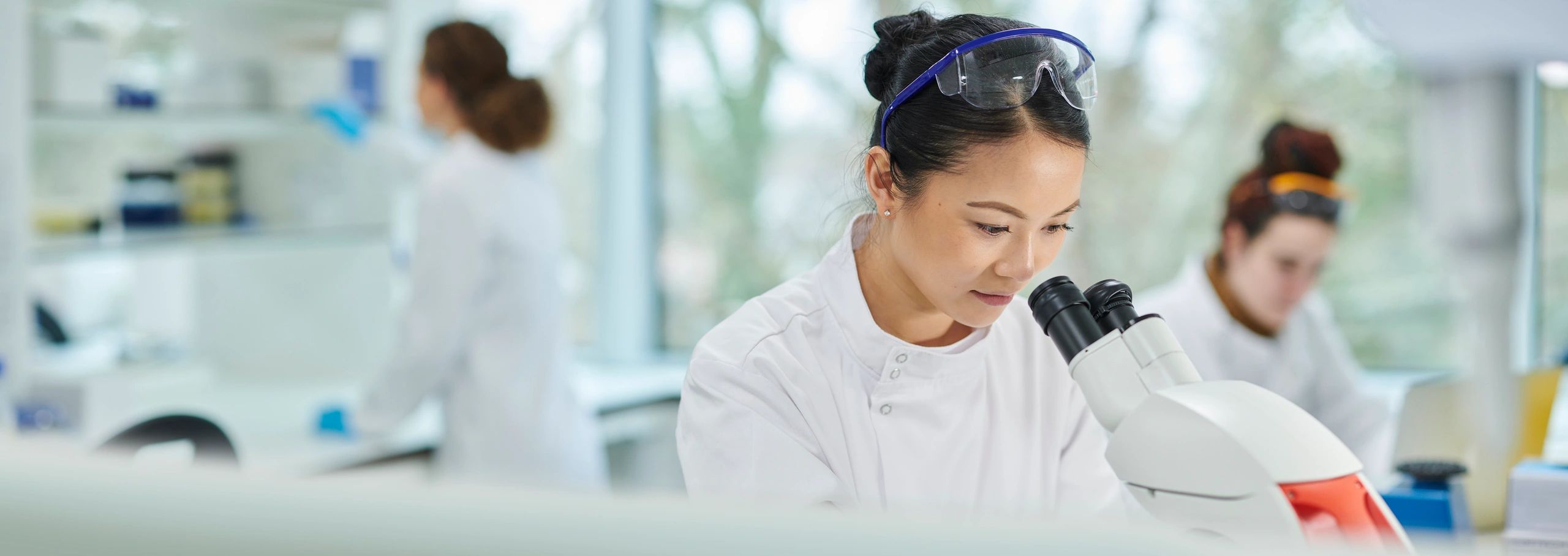 Female scientist examining samples through a microscope in a modern lab.