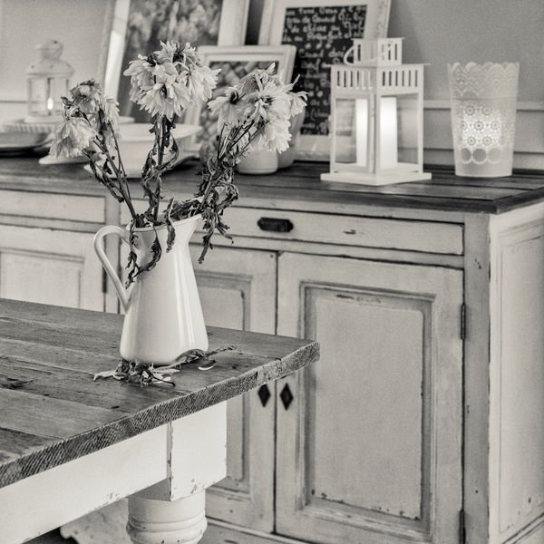 Wilted flowers in a white pitcher on a rustic wooden table.