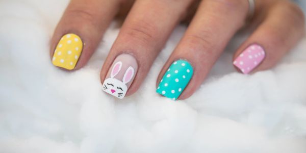 Colorful polka dot nails with a cute bunny design on one finger.