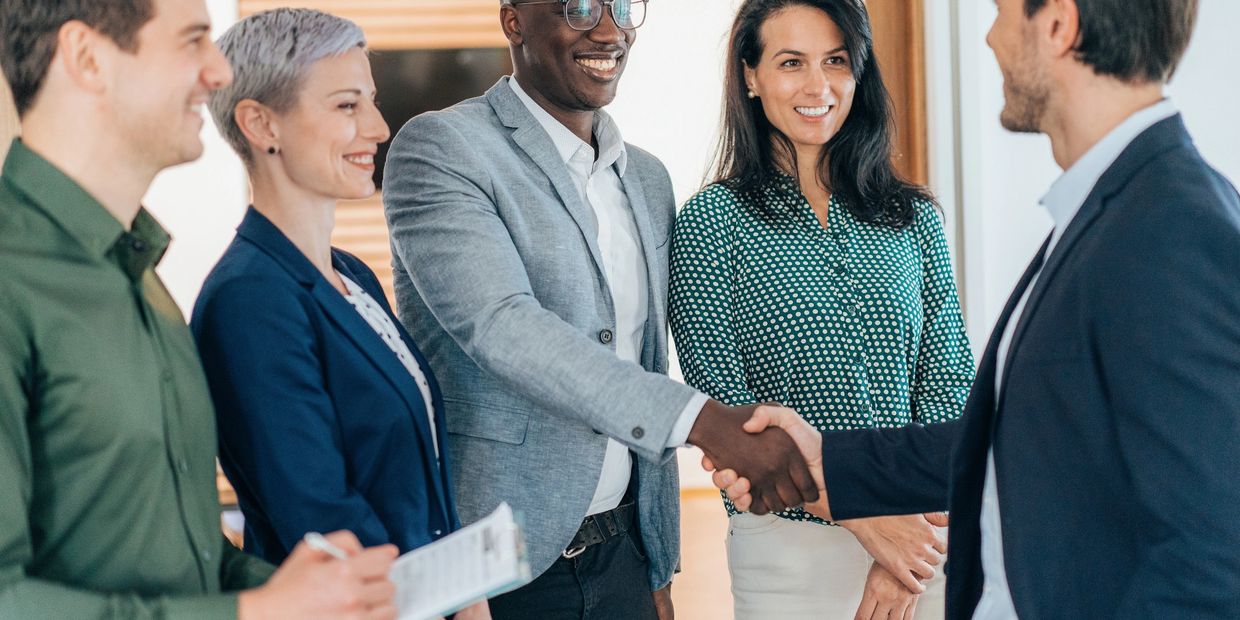 Two men shaking hands while others smile in a business setting.
