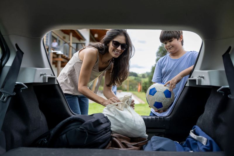 Mother picking up her son from soccer practice in her car and putting thinks in the trunk