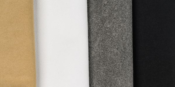 Four fabric rolls in beige, white, gray, and black colors.