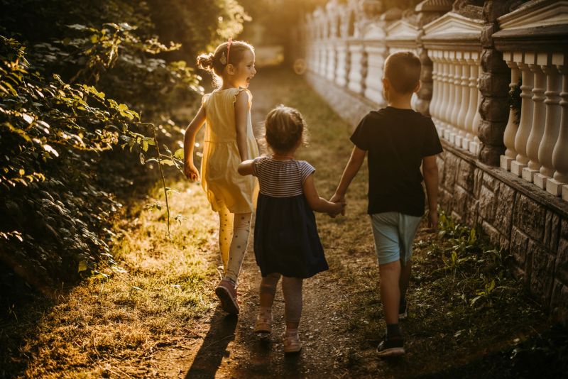 Back view of three kids while holding hands and walking