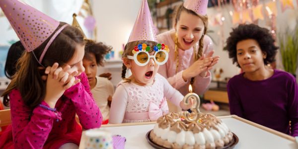 Children celebrating a birthday with a cake and party hats.