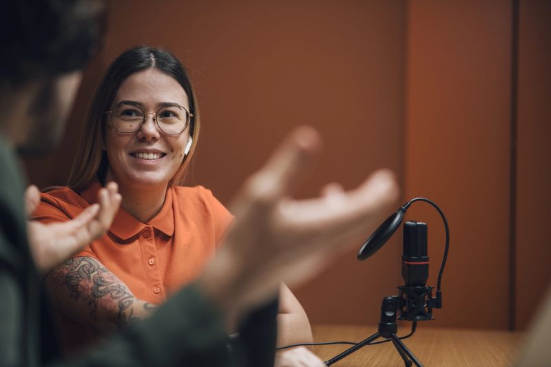 Young tattooed female smiling while being interviewed by male host in a recording studio.