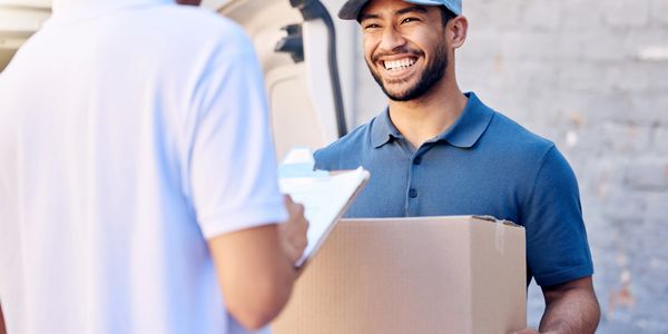 A delivery man smiling while handing a package to a customer.