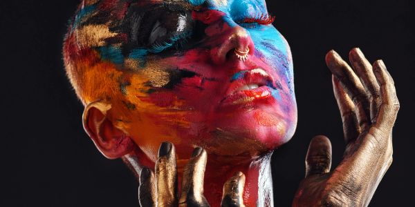 Close-up of a face painted in vibrant colors with golden hands.