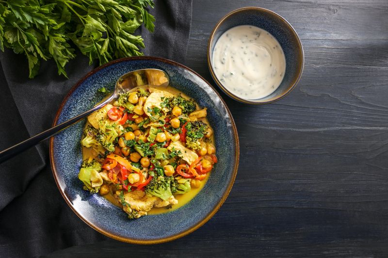 Chicken curry with chickpeas and vegetables, served with yogurt in blue bowls on a dark rustic wooden table, copy space, high angle view from above, selected focus