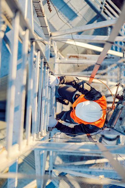 Worker in safety gear climbing a tall metal structure.