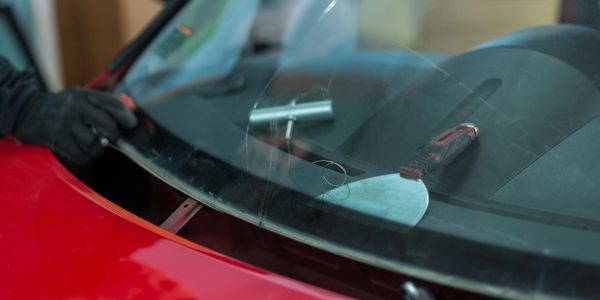 A person repairing a car windshield with tools on the dashboard.