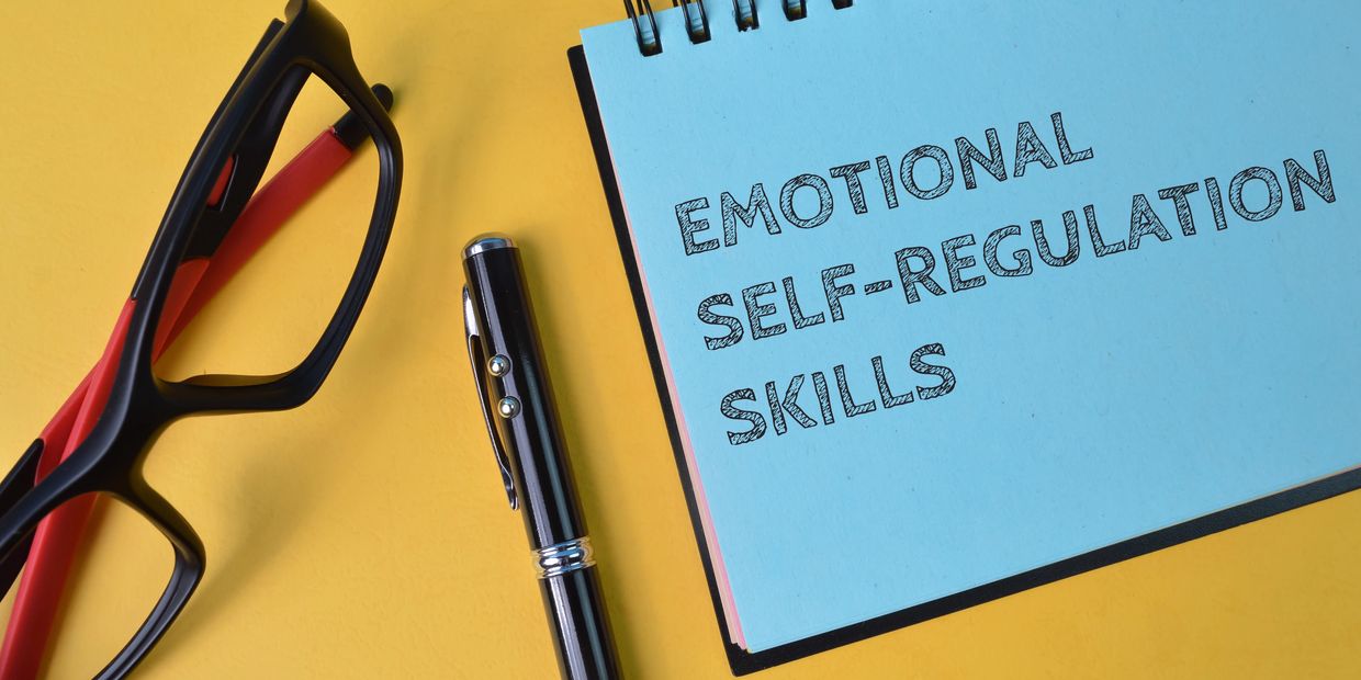 Notebook with 'Emotional Self-Regulation Skills' text, glasses, and pen on yellow surface.