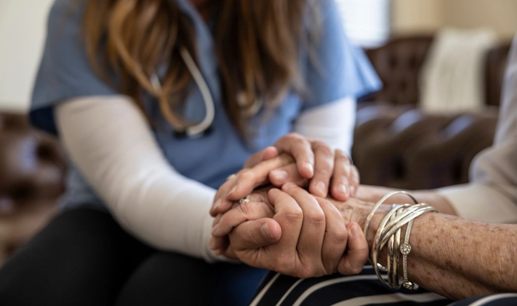 A healthcare worker gently holding an elderly person's hands.
