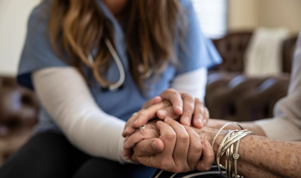 Healthcare worker holding elderly patient's hands in a comforting gesture.