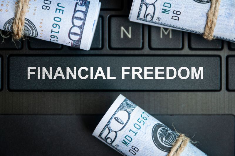 Financial freedom text on laptop keyboard with bank notes background. Finance concept
