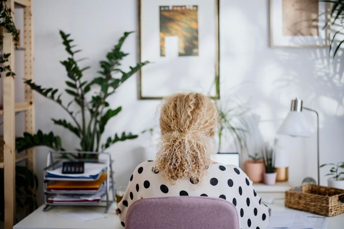 Woman with curly hair working at a desk surrounded by plants and office supplies.