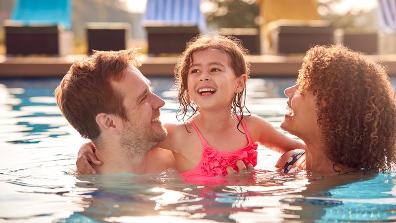 Family With Daughter Having Fun In Swimming Pool On Summer Vacation