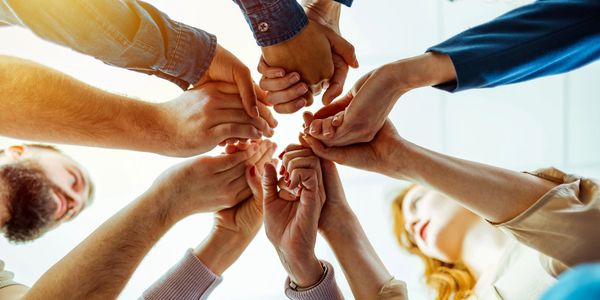 Group of people joining hands in a circle, symbolizing unity and teamwork.