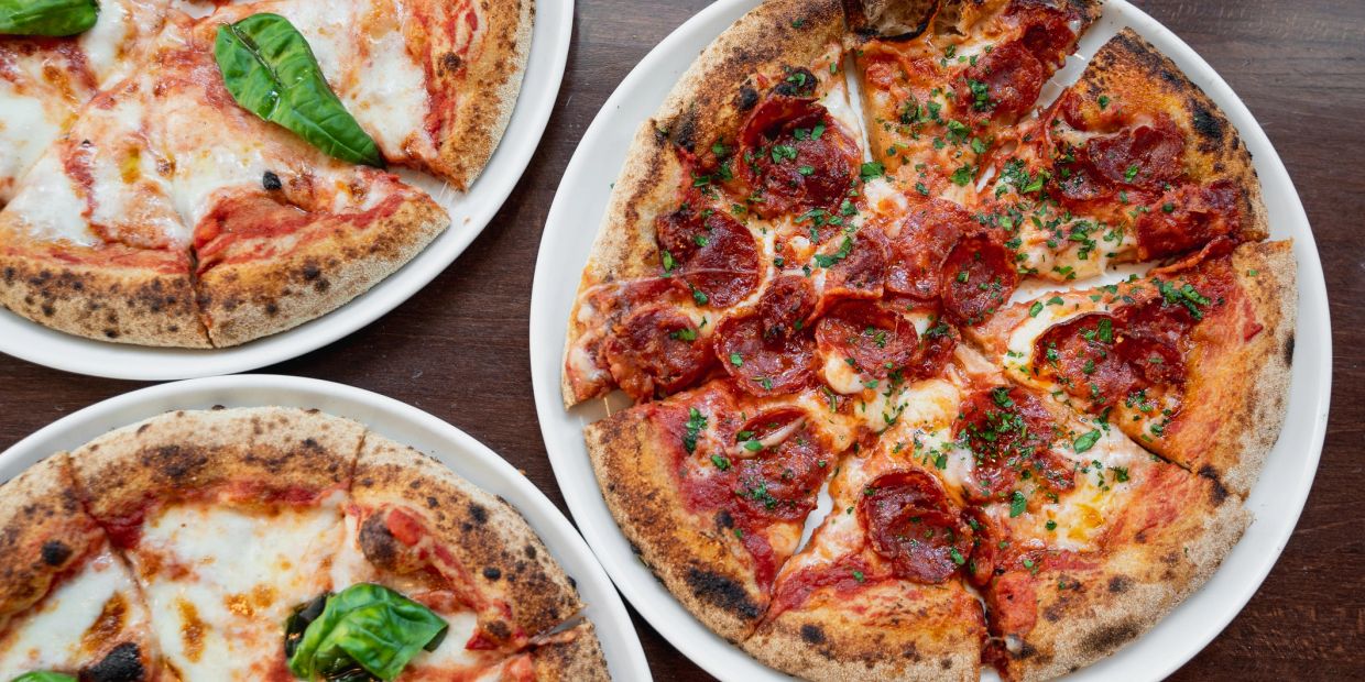 Three pizzas on white plates on a wooden table.
