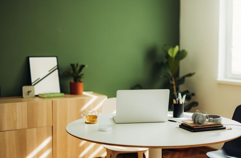 Modern office table with laptop, pens, notebook, headphones and cup of tea with no people.