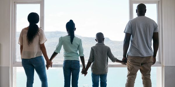 Family holding hands and looking out a large window at a scenic view.