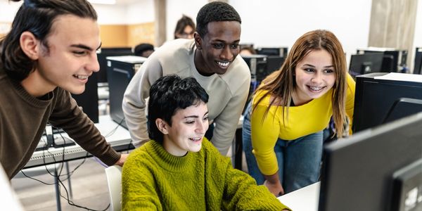 Four students happily collaborate on a computer project in a tech lab.