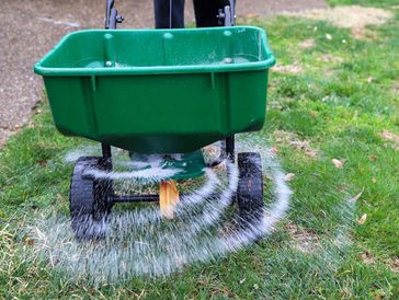 A green fertilizer spreader dispersing material on a lawn.