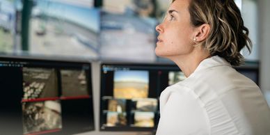 Woman attentively monitors multiple screens in a control room.