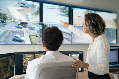 Two professionals monitoring surveillance footage on multiple screens.