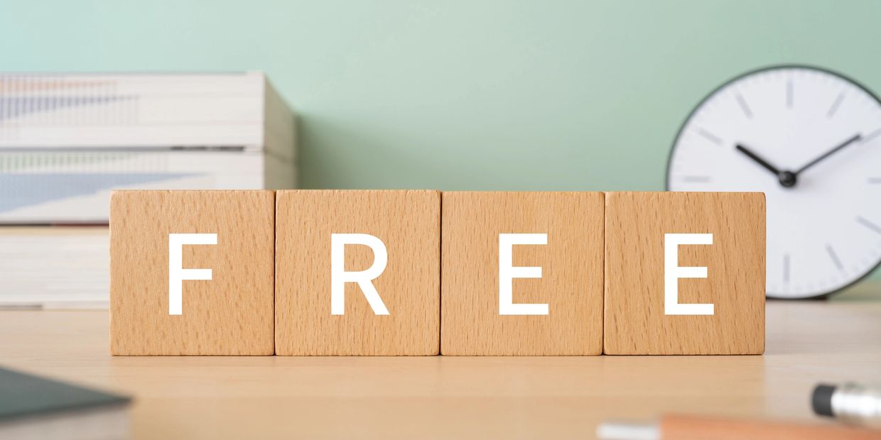Wooden blocks spelling the word FREE on a desk with books and a clock in the background.