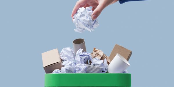 Hand tossing paper waste into a green recycling bin.