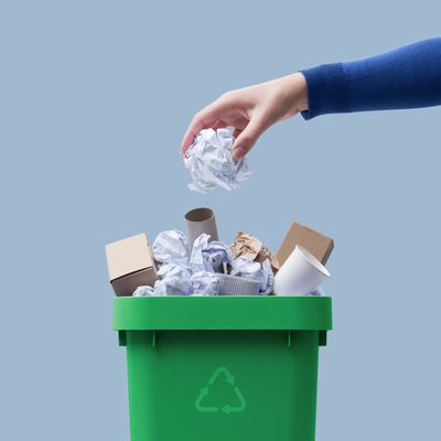 Hand tossing paper waste into a green recycling bin.