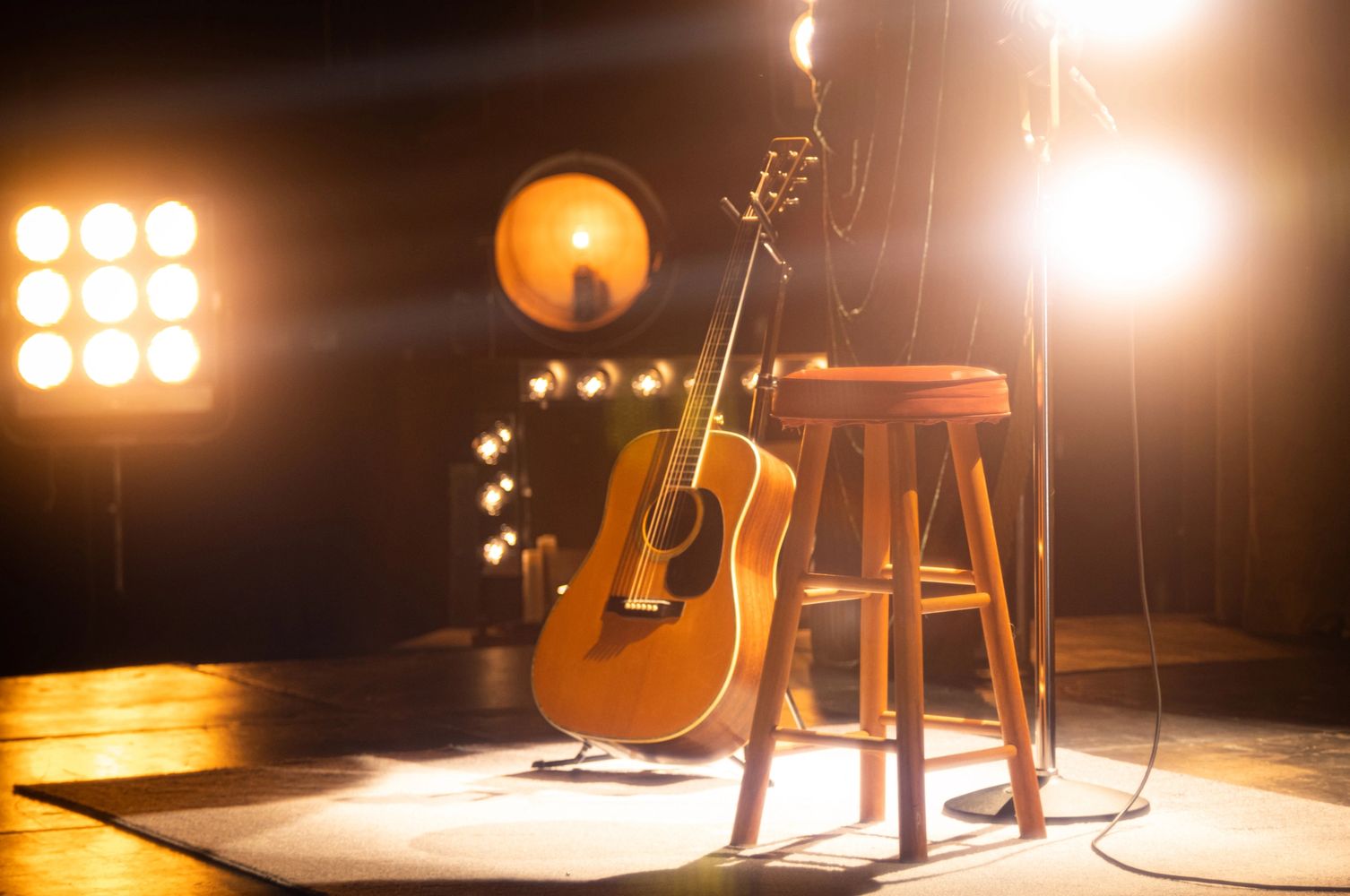 Acoustic guitar and stool on a warmly lit stage ready for a performance.