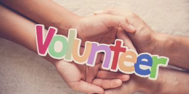 Hands holding colorful "Volunteer" letters.