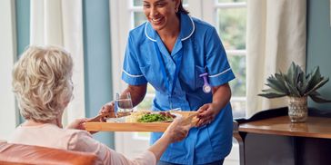 Nurse serving a meal to an elderly woman in a cozy room.